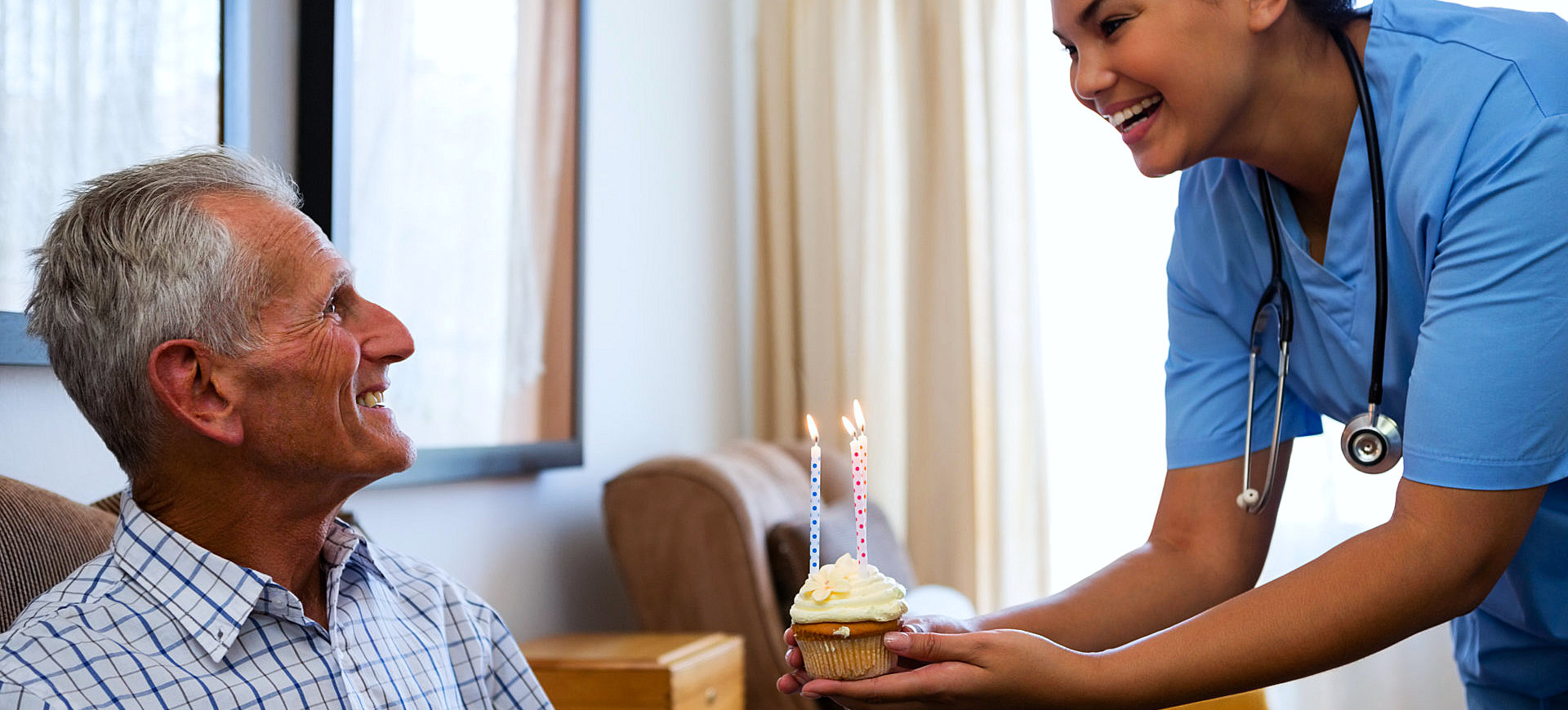 caregiver give a cupcake with candle light at top to senior man smiling